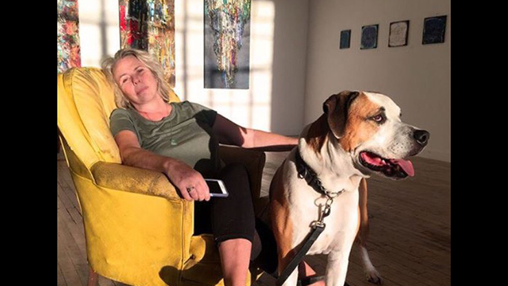 Photo of Lizbeth Mitty lying on a sofa with her dog (standing) in a gallery.